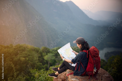 Backpacker woman sitting on top of mountain and looking map with nature background © ittipol