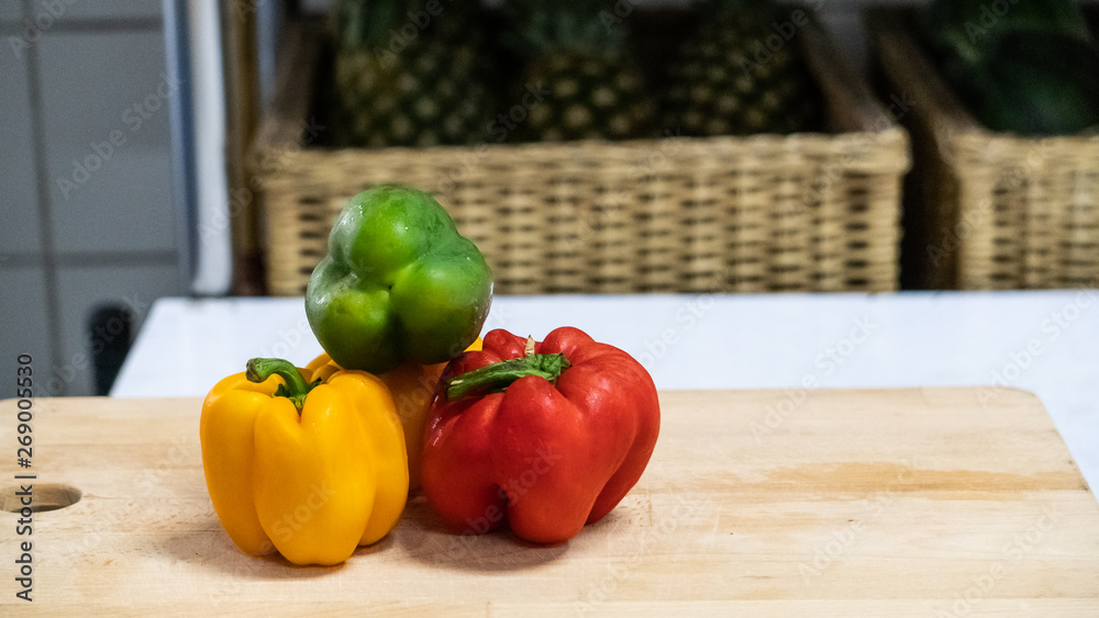 Three color peppers on a wooden board, blurred background