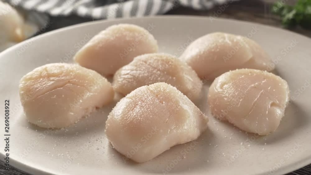 Seasoning a plate of fresh sea scallops with salt and pepper. Seasoning a plate of fresh sea scallops with salt and pepper.