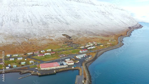 Aerial, tracking, drone shot towards the Sudavik village, snowy mountains and over the arctic sea, on a sunny spring day, at Isafjardardjup, in Westfjords, Iceland photo