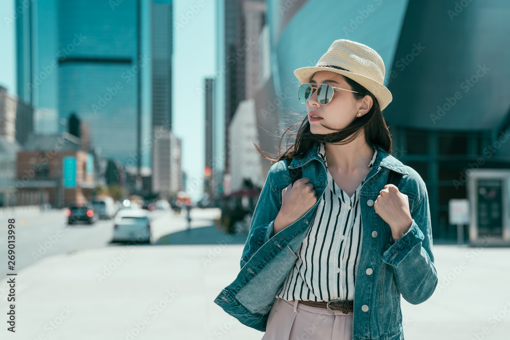 young girl tourist self guided travel in LA city walking outdoor on street. beautiful lady backpacker in straw hat and sunglasses going to visit concert hall music museum. pretty female wait taxi