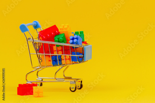 Mini shopping trolley cart full of colorful bricks on yellow background
