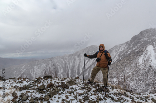 Mountaineer or extreme tourist in winter equipment stands on the background of snowy mountain peaks, relying on trekking or ski poles © evgenzz