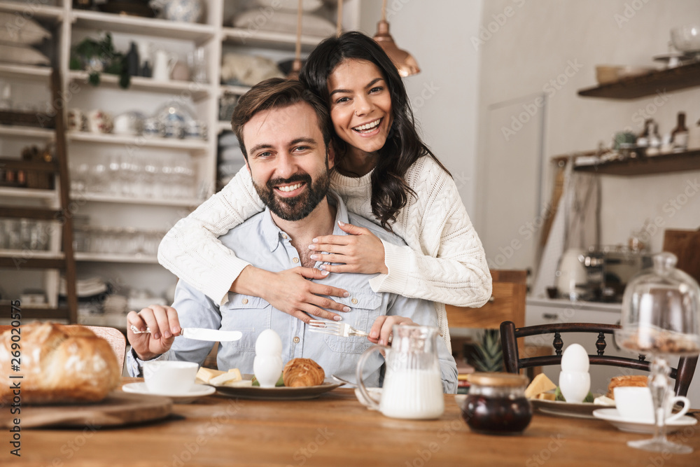 Portrait of joyful european couple eating at table while having breakfast in kitchen at home Portrait of joyful european couple eating at table while having breakfast in kitchen at home