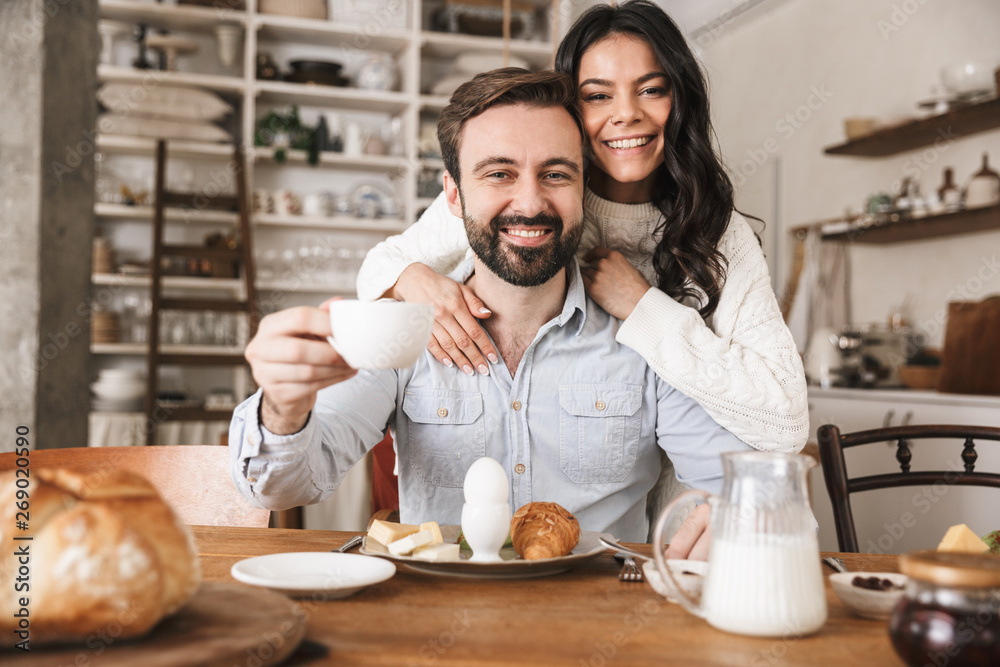 Portrait of pretty european couple eating at table while having breakfast in kitchen at home