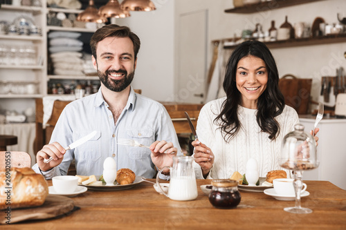 Portrait of happy couple eating at table while having breakfast in kitchen at home