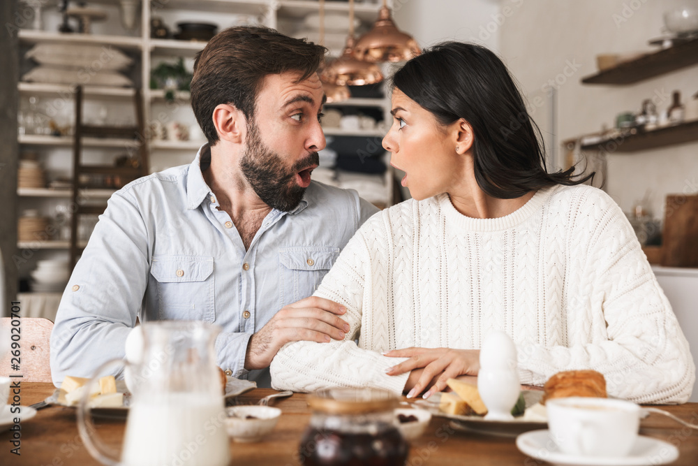 Portrait of excited couple eating together at table while having breakfast in kitchen at home