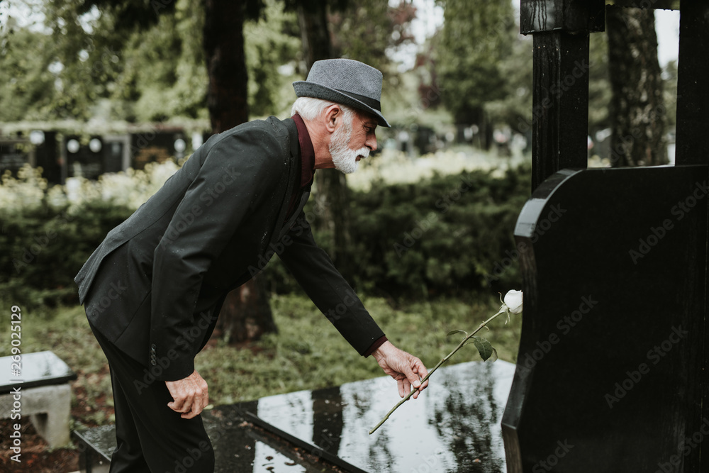 Elegant sad elderly man grieves at the grave of a loved person