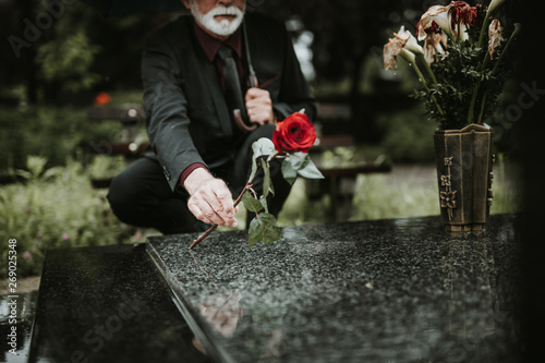 Elegant sad elderly man grieves at the grave of a loved person