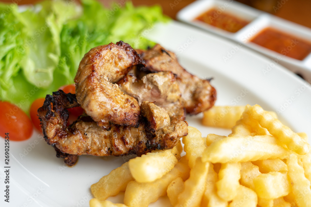 Grilled Pork and French Fries, arranged on a beautiful white food dish with salad vegetables, looking to eat Western main dishes. Popular with many