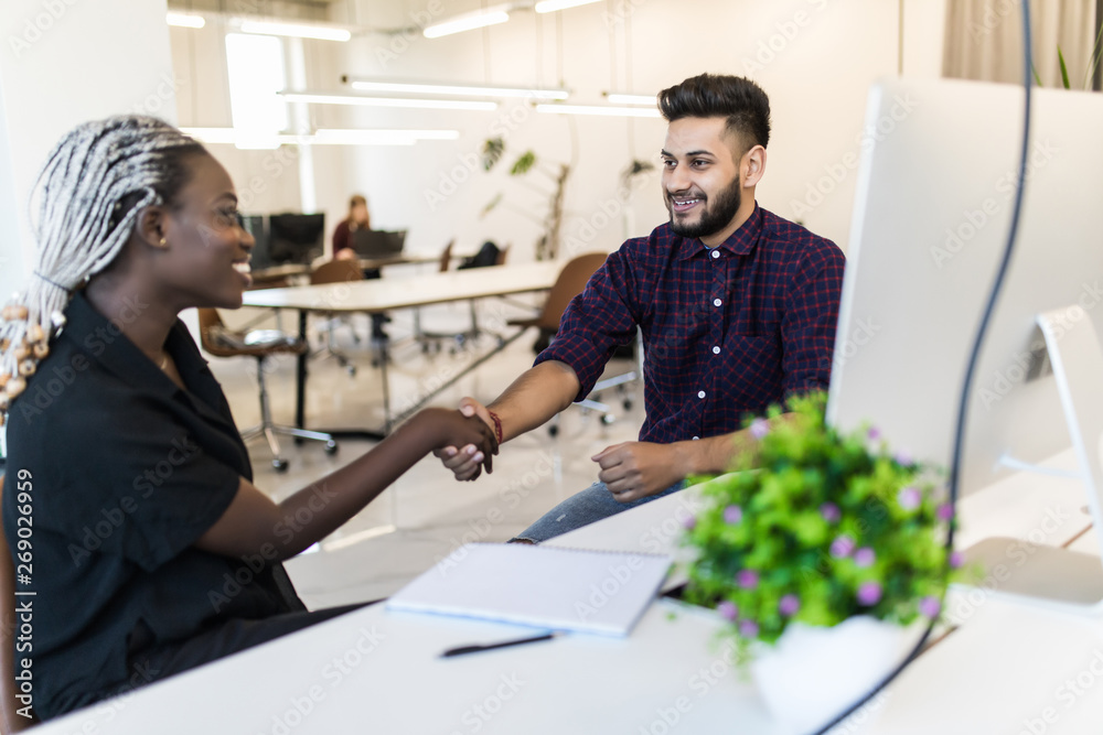Φωτογραφία Friendly smiling indian businessman and african businesswoman handshaking over the office desk after pleasant talk and effective negotiation, good relationships