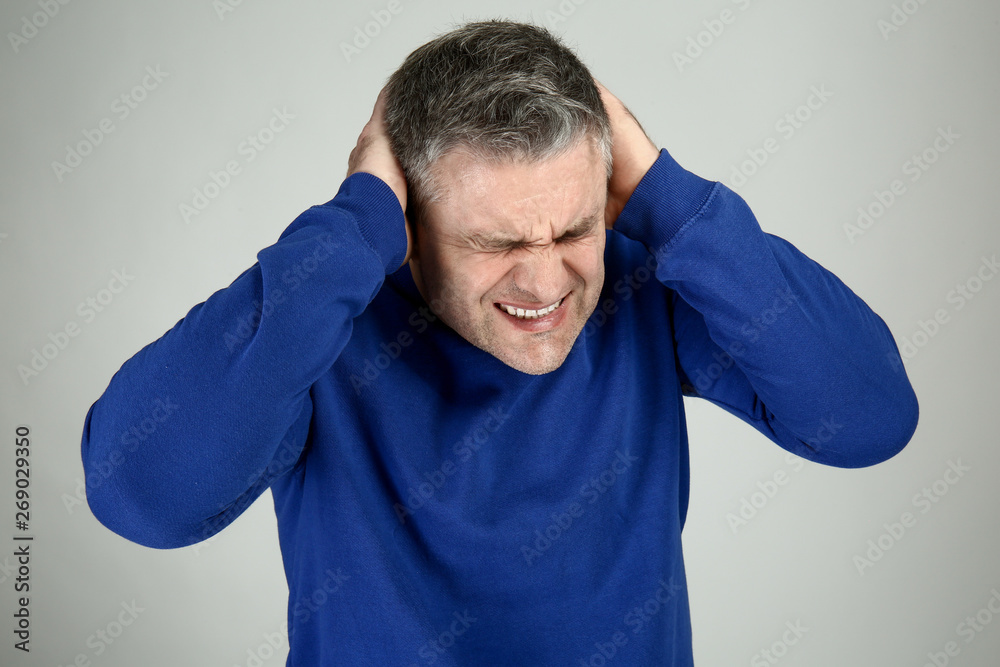 Handsome mature man suffering from terrible headache on grey background Handsome mature man suffering from terrible headache on grey background
