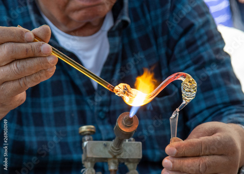 Men glassblower make handmade products under gas burner.
