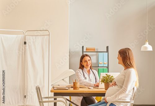 Pregnant woman is in the controlling clinic interior, woman doctor private room.