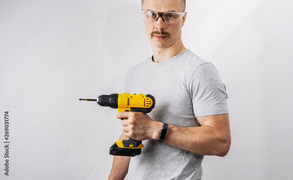 Construction: A man in protective glasses is holding a yellow electric screwdriver.