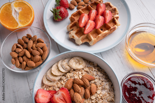 Healthy breakfast with oatmeal, waffles, fresh berry, jam, honey, nuts, on white background. Sweet delicious. Dessert