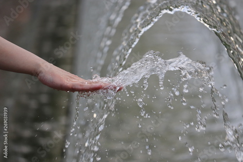 Freshness and cool, female hand in a water of the fountain. Girl washes palm in splash, concept of humidity, cooling in hot summer weather