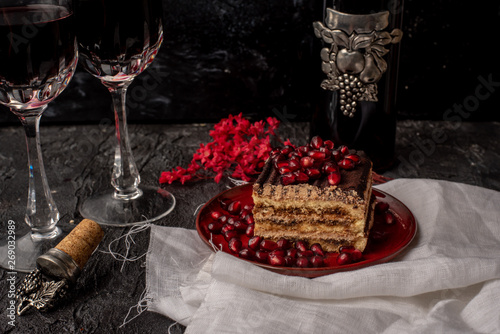 Fototapeta Naklejka Na Ścianę i Meble -  sweet, tempting tiramisu, sprinkled with red grains of pomegranate, on a black stone table, next to it red wine in crystal glasses