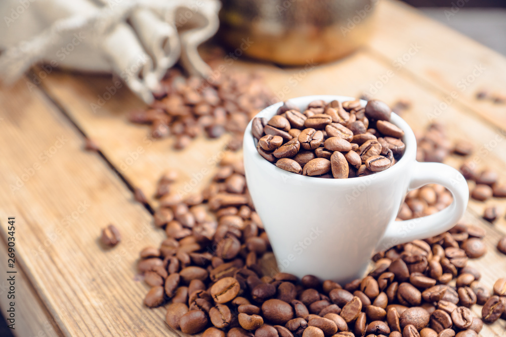 Coffee beans in white cup on the rustic wooden background. Selective focus. Shallow depth of field. Coffee beans in white cup on the rustic wooden background. Selective focus. Shallow depth of field.