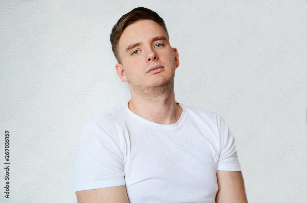 young man with blond hair on a white background in a white T-shirt looks tired and does not smile, isolated young man with blond hair on a white background in a white T-shirt looks tired and does not smile, isolated