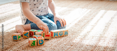 child plays with wooden blocks with letters on the floor in the room a little girl is building a tower at home or in the kindergarten.