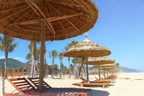 Wooden sunbeds on the beach under straw umbrella on white sand of tropical beach with palm tree.
