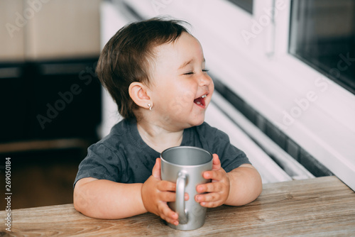 A little girl in the kitchen drinking water from a silver mug very greedily photo