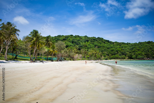 Phu Quoc island, Vietnam - March 31, 2019: White sand beach, calm sea. Rocky hills, growing palms and tropical trees. Beautiful coast of the South China Sea
