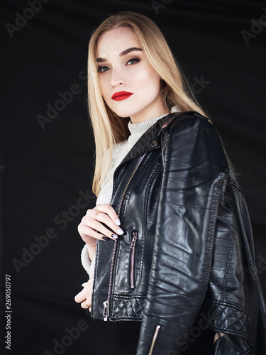 Fashion portrait stylish pretty blonde woman with bright trendy makeup red lips posing outdoor black background wearing a rock black style leather jacket on her shoulder having fun in city.