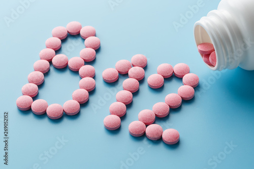 Pink round vitamins B12 shaped pills on a blue background spilled from a white can photo