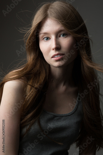 beautiful redhead model girl with long hair in the Studio on a gray background in a t-shirt