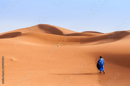 A person walks through sand dunes in the Sahara / A person in traditional clothing walks through the sand dunes in the Sahara, Morocco, Africa. © ub-foto