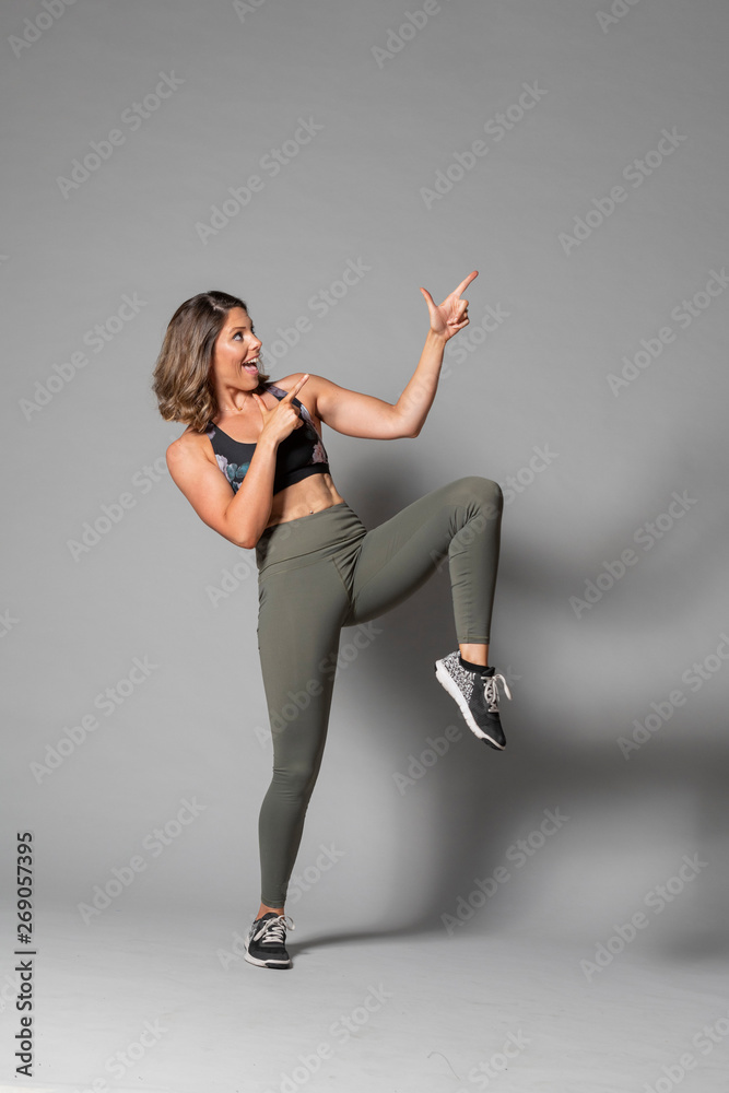 Obraz premium Beautiful caucasian fitness Models does pointing gestures for product or icon placements on a gray background. 