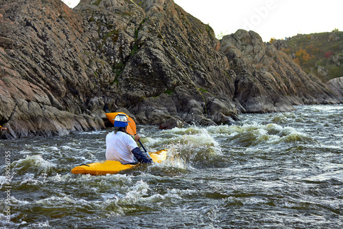 A man dressed as a monster big pasta (macaroni) in kayak paddling on rapid whitewater river at dusk. Funny costume sports show on the water © watcherfox