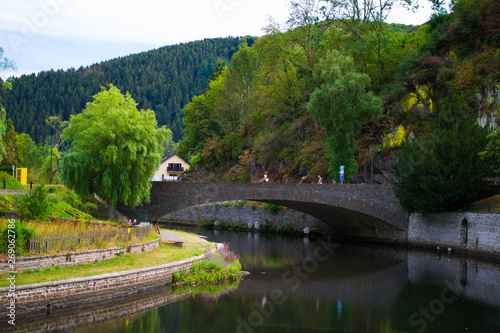 Old stone bridge over Sure river with a walkway through the riverside and mountain and trees at the background. Esch Sur Sure, Luxembourg photo