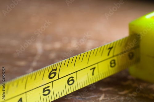 Tape measure tool in yellow inches and centimeters on wooden background