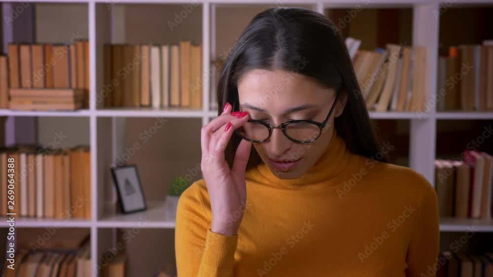 Portrait of pretty brunette female teacher in glasses smiling happily into camera and flirting with it at the library. Portrait of pretty brunette female teacher in glasses smiling happily into camera and flirting with it at the library.