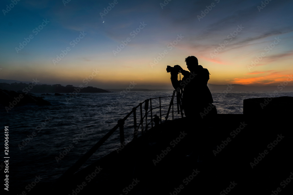 silueta de fotografo en puerto durante el anochecer usando tripode