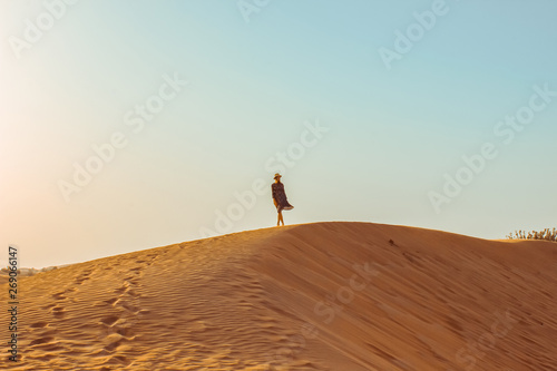 Young beautiful girl in a long dress and a hat in the middle of the desert during the daytime