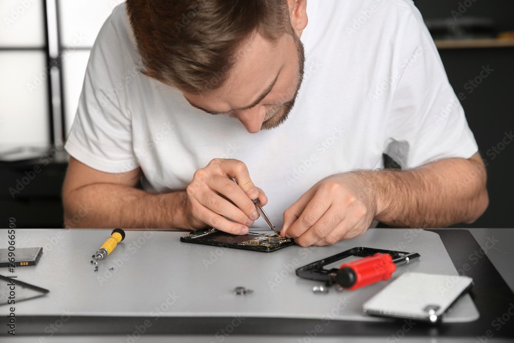 Naklejka premium Technician repairing mobile phone at table in workshop