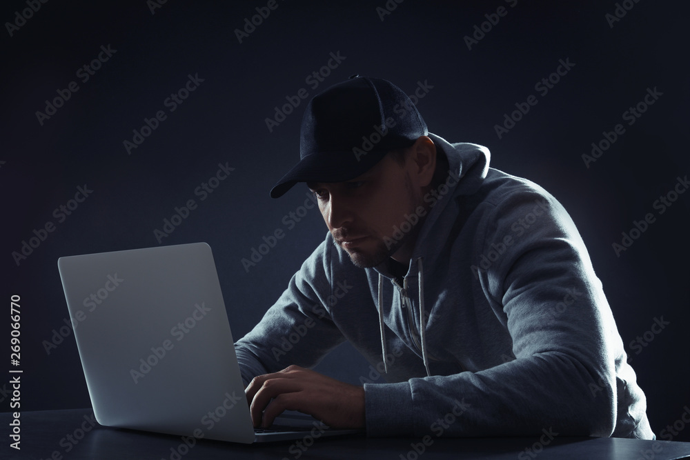 Man using laptop at table on dark background. Criminal activity Man using laptop at table on dark background. Criminal activity