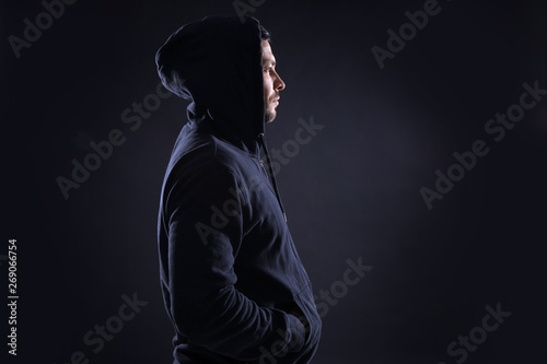 Mysterious man in hoodie on dark background. Dangerous criminal