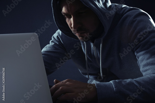 Man using laptop on dark background. Criminal activity