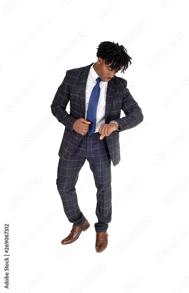 Relaxed black man standing in a suit looking at his watch Relaxed black man standing in a suit looking at his watch