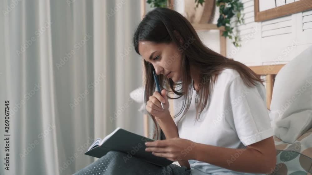 Pretty woman sits on bed and makes notes in daily planner, slow motion. Pretty woman sits on bed and makes notes in daily planner, slow motion.