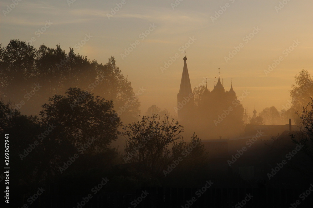 Trees and church silhouettes in misty summer morning