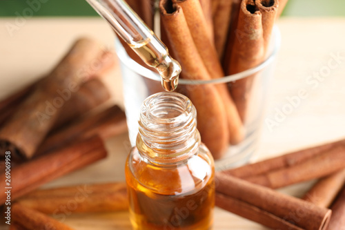 Pipette with essential oil over bottle and cinnamon sticks on table, closeup