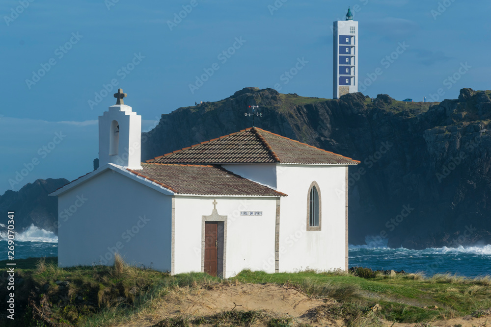 iglesia en la costa con faro al fondo sobre una montaña con grandes acantilados