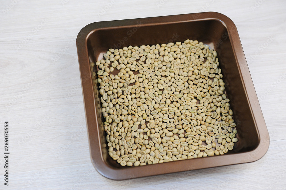 Raw unroasted green coffee beans in a baking tray before home roasting in the oven top view Raw unroasted green coffee beans in a baking tray before home roasting in the oven top view