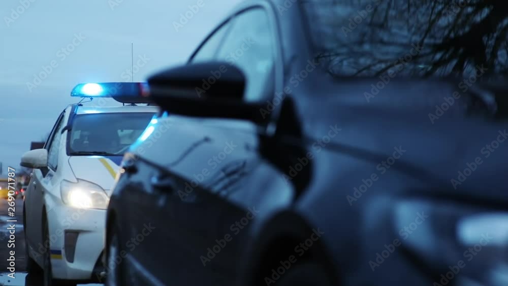 Close of the car fined for overspeeding standing on the roadside. Police car with lights turned on behind the driver. Close of the car fined for overspeeding standing on the roadside. Police car with lights turned on behind the driver.